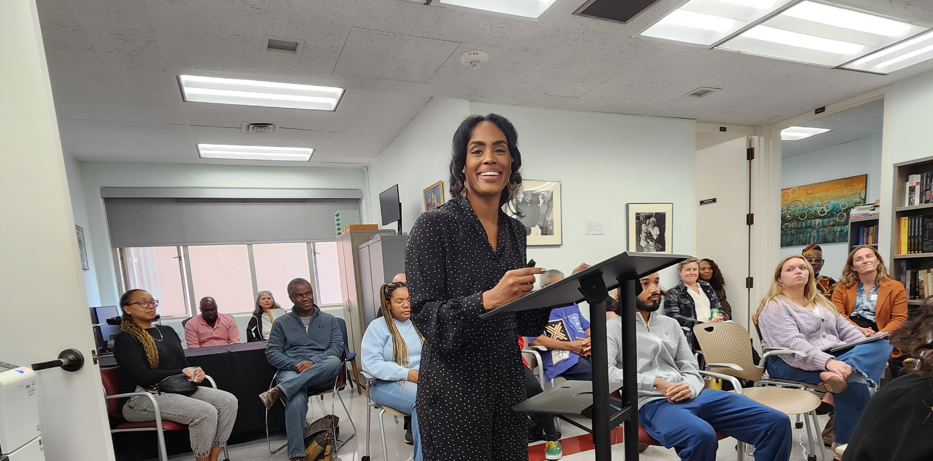Pedagogy symposium presenter smiles at camera, audience in background