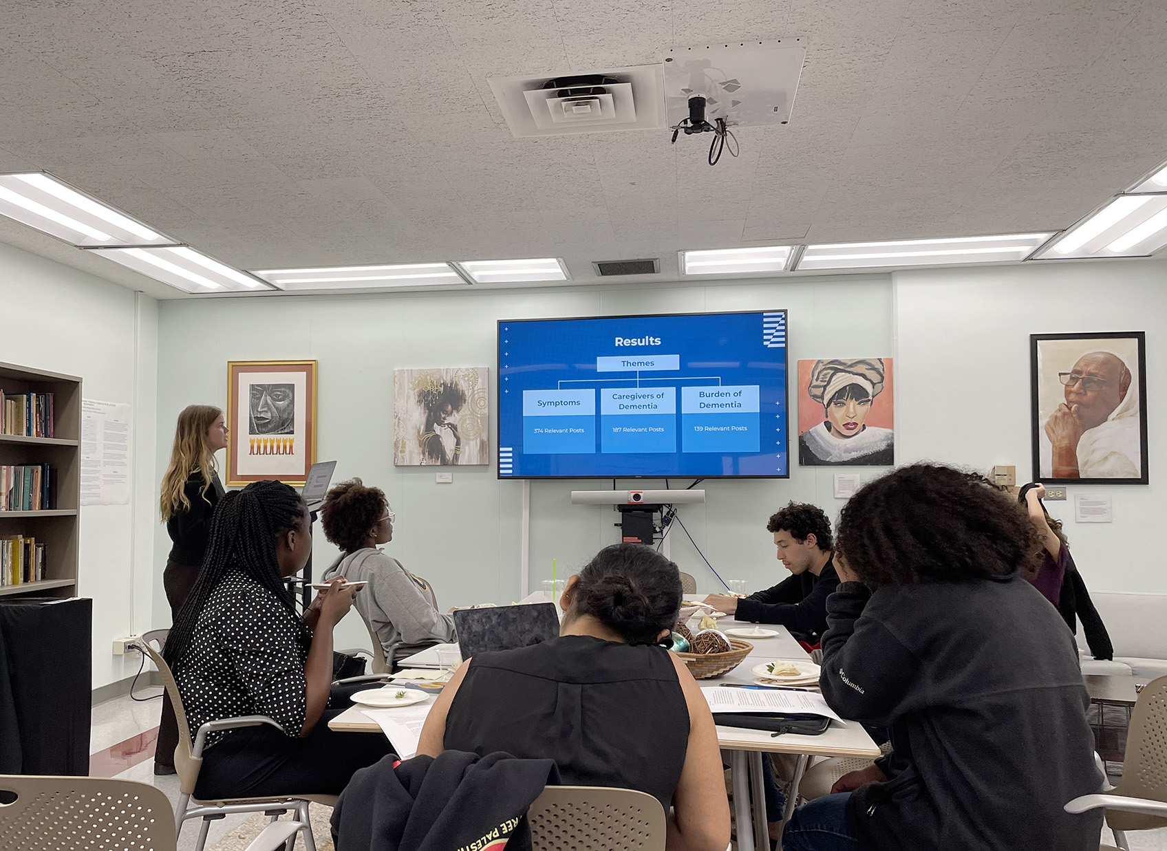 Female student presenting to peers in room with screen hanging on wall