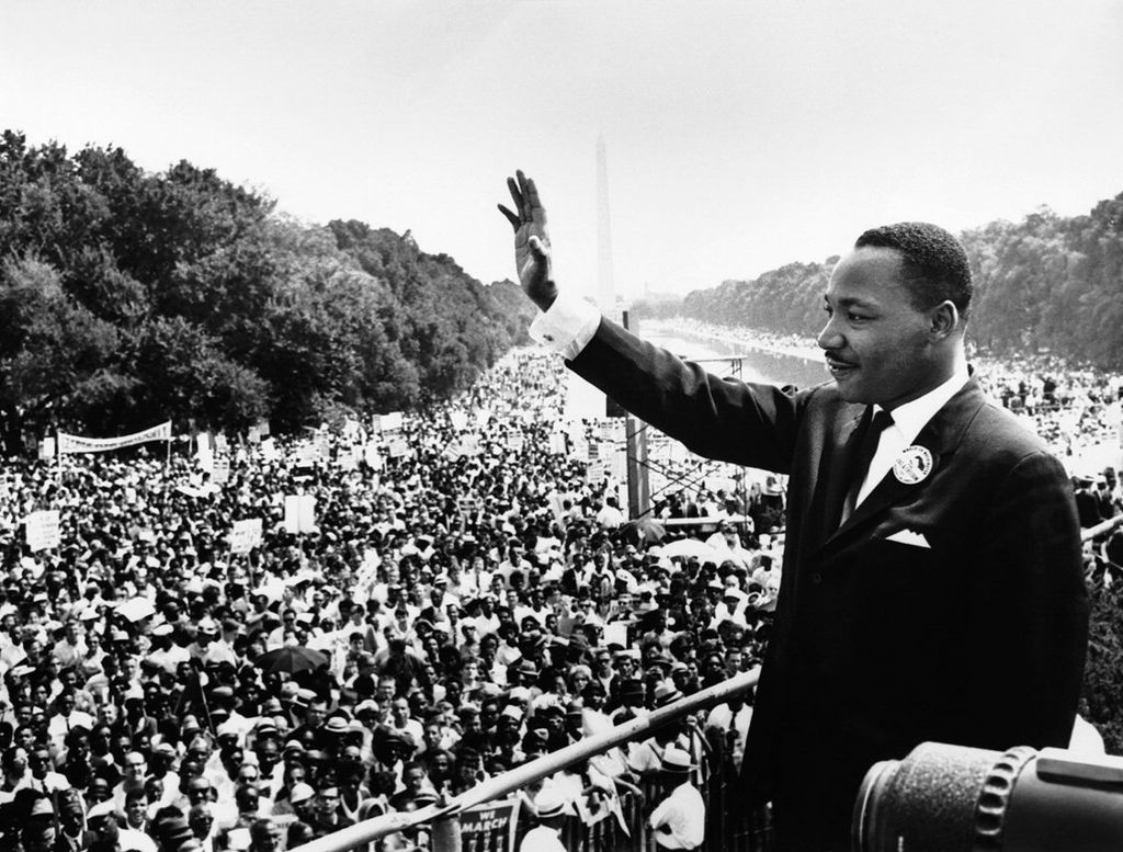 martin luther king waving his hand at a large croud