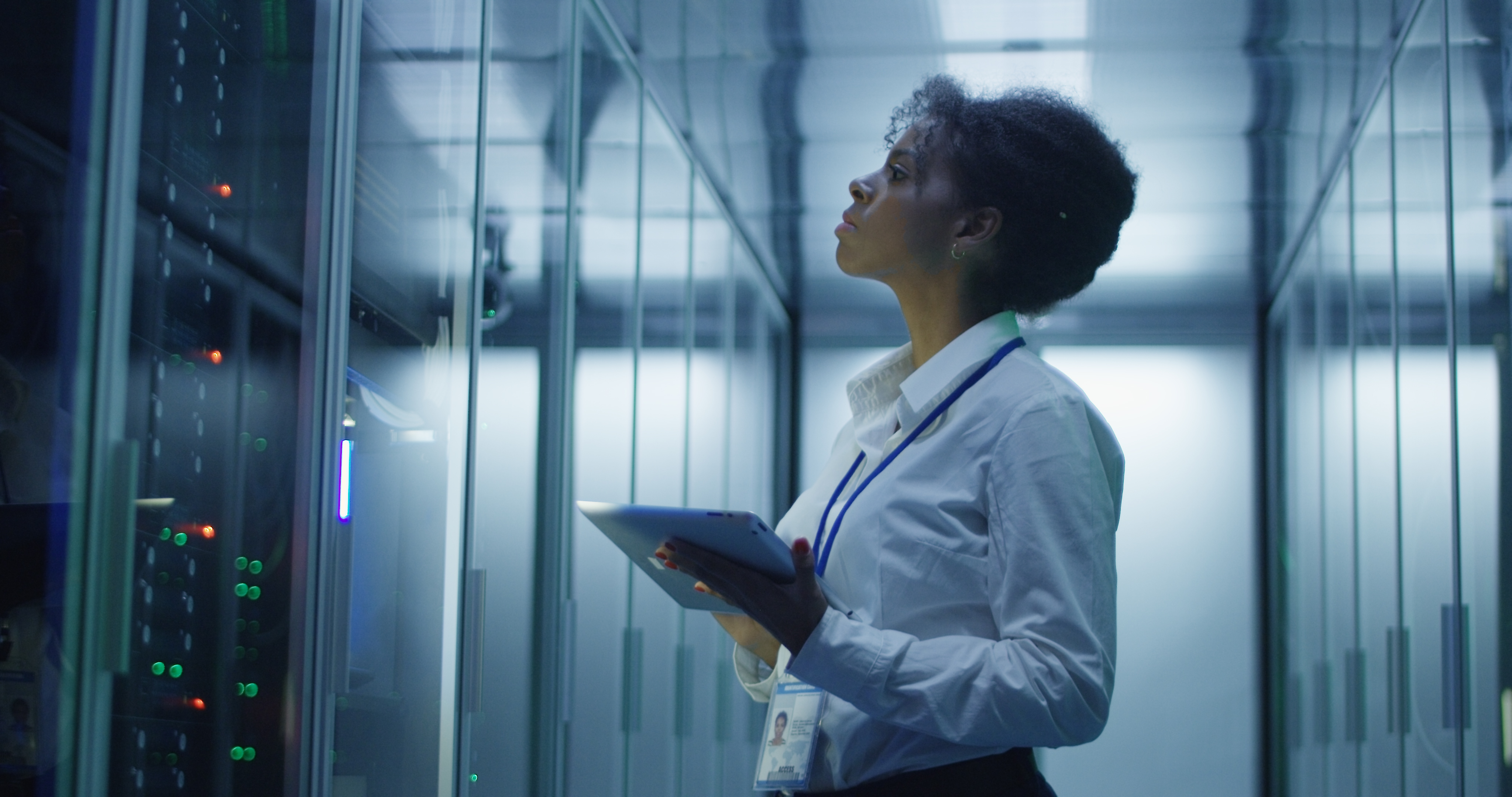 Formal African American woman using tablet while working with server rack in contemporary data center hallway