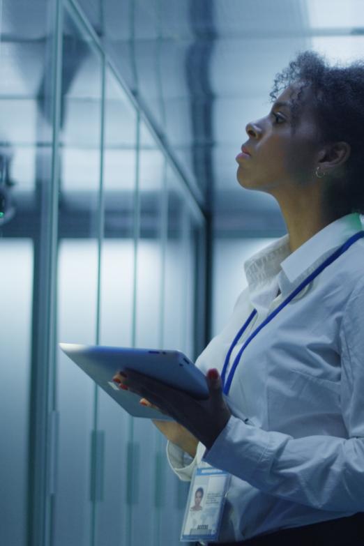 Formal African American woman using tablet while working with server rack in contemporary data center hallway  