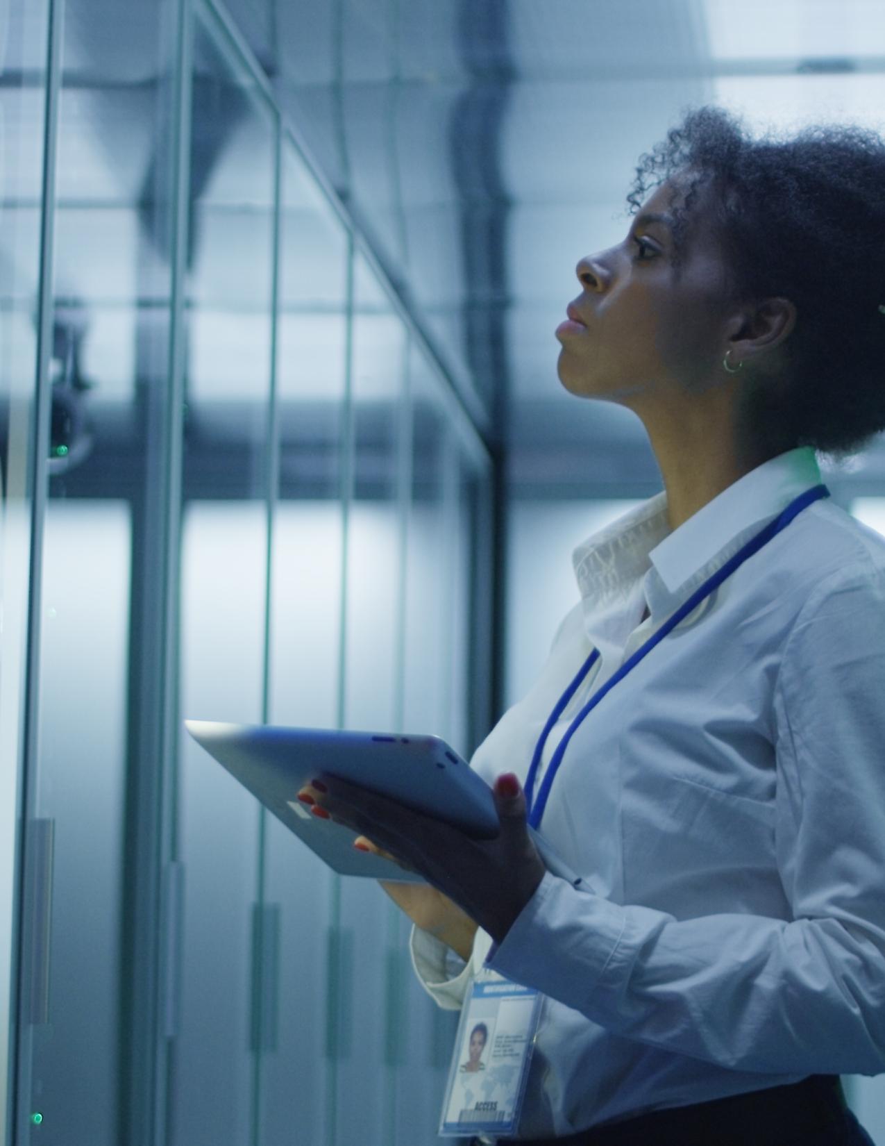 Formal African American woman using tablet while working with server rack in contemporary data center hallway   
