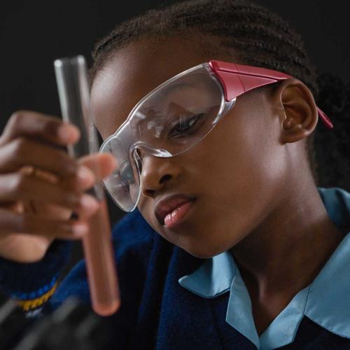 Close-up of a young girls wearing goggles while looking at a vial in science class